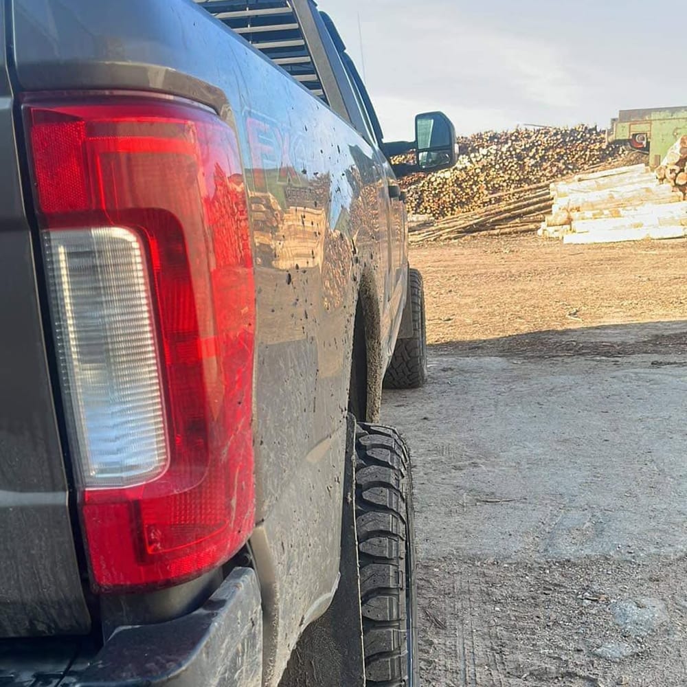 Quart arrière d’un Ford F-250 chaussé de pneus tout-terrain, devant des billots empilés.