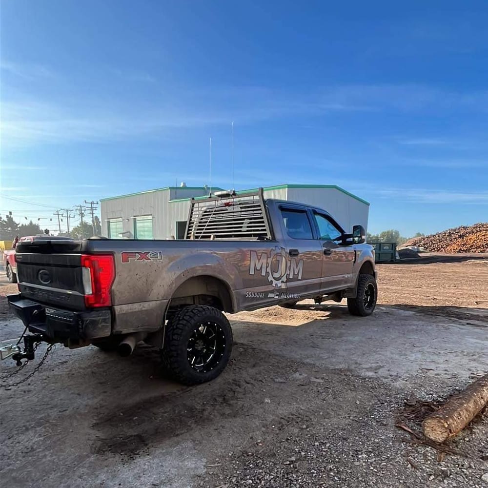 Ford F-250 FX4 gris soulevé, sur des mags noirs et des pneus tout-terrain, devant une cour à bois.