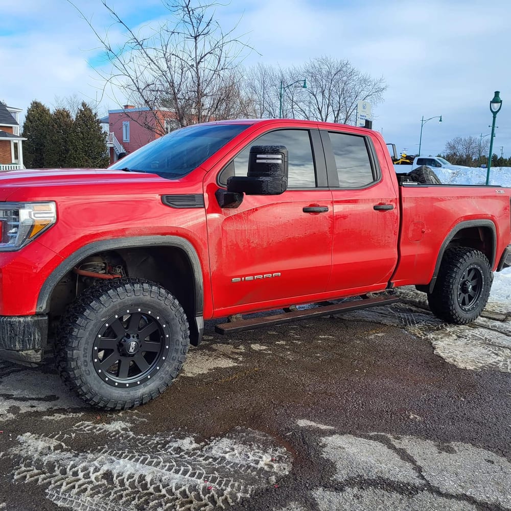 GMC Sierra rouge de profil, stationné à Roberval, sur des mags noirs et des pneus tout-terrain.
